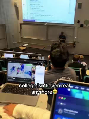 A person is sitting in a lecture hall, facing away from the camera. The foreground shows a laptop and a smartphone. In the background, a large screen displays what looks like code. The overall composition suggests a discussion of modern college academics.