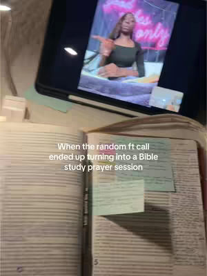 The image shows an open book laid on a table. A tablet displays a video call featuring a person, with text overlaid. The image uses warm lighting and appears to be in a home setting.