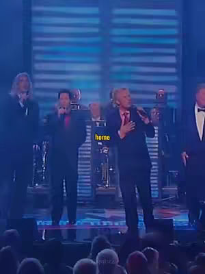 A stage is lit in blue, with a group of men singing. A yellow text box with the word "home" is overlaid near the center.