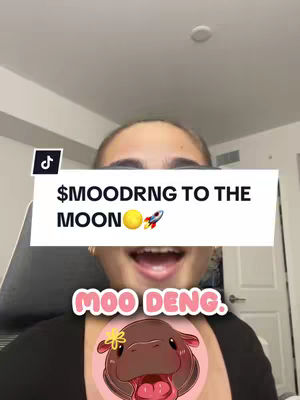A young woman with fair skin is smiling and looking directly at the camera. Above her head is a white rectangle with the text '$MOODRNG TO THE MOON' in a bold, sans-serif font, along with a sun and rocket ship emoji. Centered on her face is a pink circle containing an image of a cartoon hippo with a yellow flower and the text 'MOO DENG'.