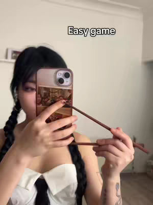 A young woman with pigtails is holding chopsticks and a phone in front of her face. The phone covers most of her face.
