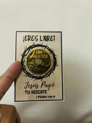 A hand holds a card with a gold coin in the center. Around the coin is a black thorny circle. The text on the card reads '¡ERES LIBRE!', 'Jesús Pagó' and 'TU RESCATE, I PEDRO 1:18-19'. The background is a light cream color.