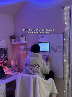 The image shows a person from the back, sitting in a room with a desk and a whiteboard. The person is wearing a hoodie with the words 'Atelier Original' on the back. There’s a laptop on the desk. The room is lit with purple lights. Text overlayed on the image says 'this is the function bc I decided to save lives for living.'