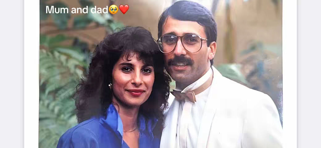 A vintage photo featuring a smiling woman and a man with glasses, likely a couple. The woman has dark, curly hair and is wearing a blue top. The man has a mustache, wears round glasses, and a bow tie over a white blazer