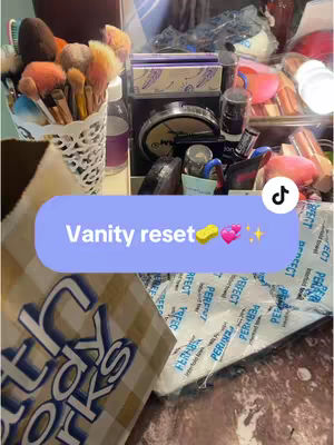 The image shows a close-up of a vanity setup with a light blue overlay. A variety of makeup items and brushes are visible. At the bottom of the picture, partially obscuring the view, is a shopping bag.