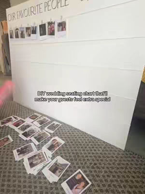A large white board leaning against a wall is the main focus, featuring a seating chart display for a wedding. Small polaroid photos are clipped to the top of the board which has the words 'OUR FAVORITE PEOPLE' written in a fancy font. A pile of similar unclipped photos sits in front near the bottom of the board on a patterned carpet. Text overlayed on the image reads 'DIY wedding seating chart that'll make your guests feel extra special'.