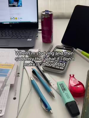 A close-up, slightly overhead shot of a desk scattered with study materials. The items include a laptop displaying a webpage, a can of Red Bull, a calculator, pens, highlighter, papers, and a tablet. The composition is cluttered yet organized, with a focus on the various objects associated with studying.