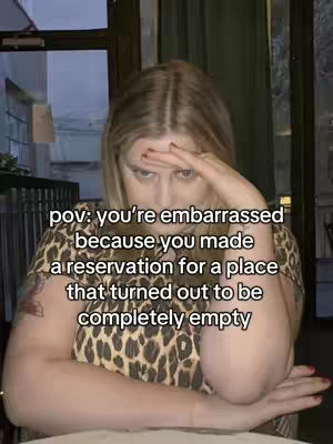 A woman with long blonde hair is looking directly at the camera, raising her right hand to her forehead in a gesture of exasperation. The text overlay is in white, and the woman is wearing a leopard print top, with a restaurant or bar setting in the background. The lighting is soft, and the overall composition conveys a sense of embarrassment or frustration.