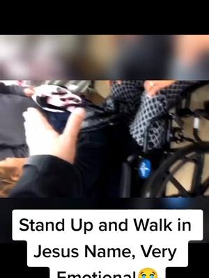A video frame showing a person's hand pointing towards a person in a wheelchair. Text overlayed at the bottom of the frame reads, “Stand Up and Walk in Jesus Name, Very Emotional.” The background is slightly blurred and appears to be indoors.