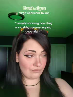 A selfie-style shot featuring a woman from chest up, set against a green-tinted background. She has dark hair, dark eyes, and is wearing makeup. Text overlays are present at the top with astrological details and explanations. The overall lighting seems to be a bit artificial, possibly from internal sources.
