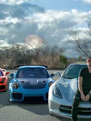 A group of supercars parked on pavement, with a man leaning on the hood of a silver car. The sky is overcast with prominent clouds. From left to right, there is an orange car with red details, a blue car, and a silver car which the man is leaning on. The man wears sunglasses, a black t-shirt, and dark pants.
