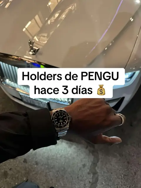 A person's hand with a luxury watch is in the foreground; behind, part of a white Rolls-Royce is visible.