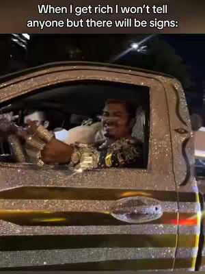 The image shows a man in an elaborately decorated, diamond-encrusted car, giving a view out of the window. The man has jewelry on, and it is nighttime.