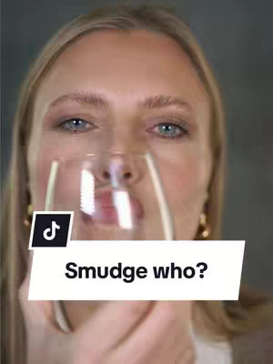 A close-up shot features a woman holding a wine glass to her lips, with only her face visible. A text overlay reads 'Smudge who?' in a white rectangular box. The background is blurred, with soft neutral tones.