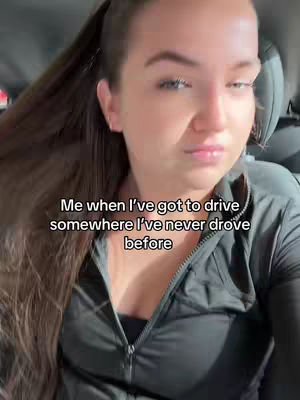 A selfie-style shot taken from inside a car, featuring a woman with long brown hair pulled back in a ponytail. She is positioned in the driver's seat, wearing a dark top. The image has text overlaid on it.