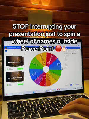 The image shows a laptop displaying a wheel-of-names app within a PowerPoint presentation. The scene is lit dimly.