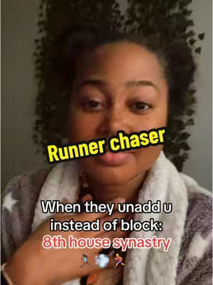 A selfie-style shot featuring a Black woman. She has a neutral expression, and her face is partially obscured by a yellow text overlay. She is wearing a light-colored, patterned garment. The background is out of focus, showing a wall of green foliage, and a white or gray blurred background.