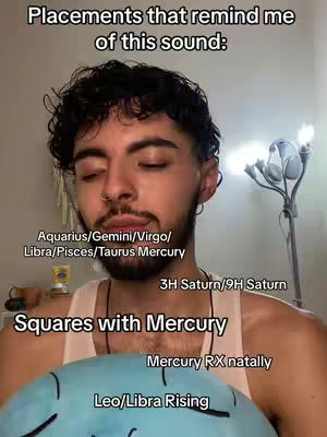 A man is shown centered in a selfie-style shot. The background is slightly blurred, suggesting an indoor setting. Text overlays include descriptions of zodiac placements. The man has curly dark hair, a nose ring, and a neutral expression. A small table and a lamp are visible in the background.