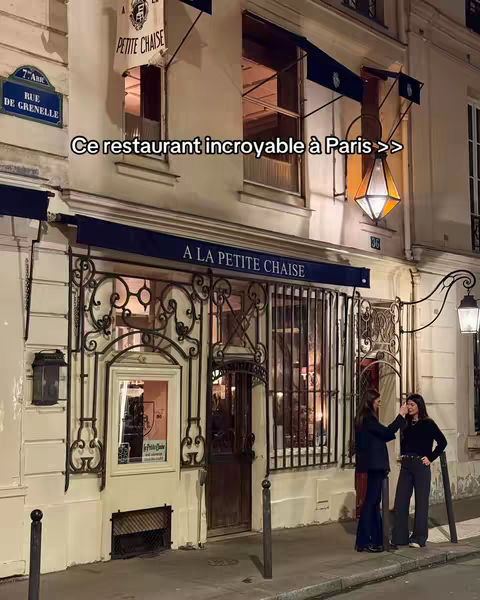An exterior nighttime shot of a Parisian restaurant, 'La Petite Chaise.' The building has a classic facade with wrought-iron detailing above the entrance. Two women stand near the entrance, and the hook text 'Ce restaurant incroyable à Paris' is overlaid on the image.
