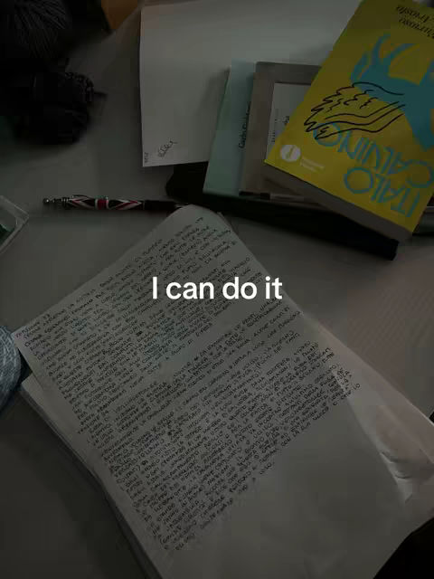 The cover image shows a desk with a notebook, pen, and books scattered on it. The foreground includes a handwritten notebook page with text. On the right is a yellow book with visible text, and partially visible are other items like stationary and what appears to be a photograph or a frame. The lighting appears to be natural, creating shadows.