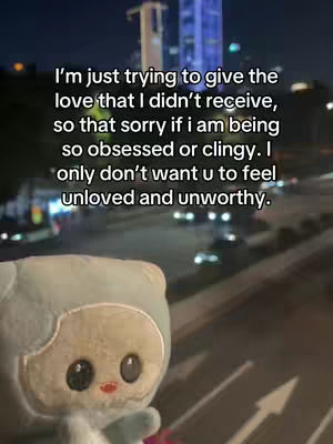 The image features a softly blurred night scene with city lights and a focus on a hooded plush toy in the foreground. Text overlays appear to express emotional sentiments. The overall effect is intimate and introspective.