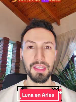 A man with dark hair and a beard is centered in the frame, looking directly at the camera. The background includes exposed wooden ceiling beams and a brick wall. A text overlay at the bottom reads 'Luna en Aries' in a red box.