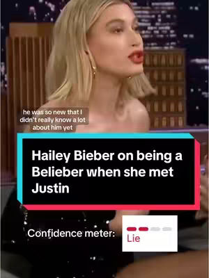 The image captures Hailey Bieber in a close-up shot, mid-speech, against a blurred background featuring what seems to be a studio setting. A text overlay includes the title: 'Hailey Bieber on being a Belieber when she met Justin' and a meter indicating 'Lie'.