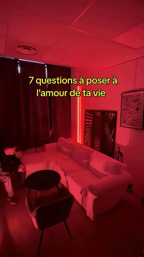 A room bathed in red light, featuring a white sofa, a black table, and a dark-colored chair. Text in yellow displays the title of the video. A person stands in the background.