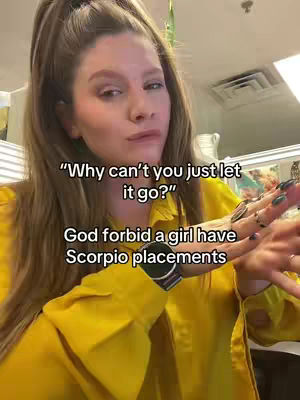 A woman with long, light brown hair in a half-up style peers at the camera with a slight frown. She wears a yellow, collared shirt, and her hand, adorned with multiple rings and a watch, is raised. Text overlays appear on the image.