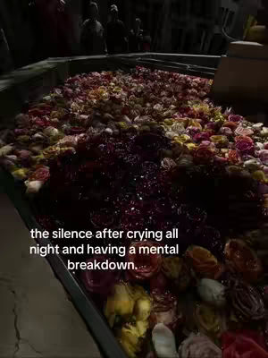 An overhead shot shows a black container overflowing with colorful rose petals. In the center, there is a large area of dark, crushed petals. The background is out of focus, with some blurry figures in the distance. Text is overlaid on the image.