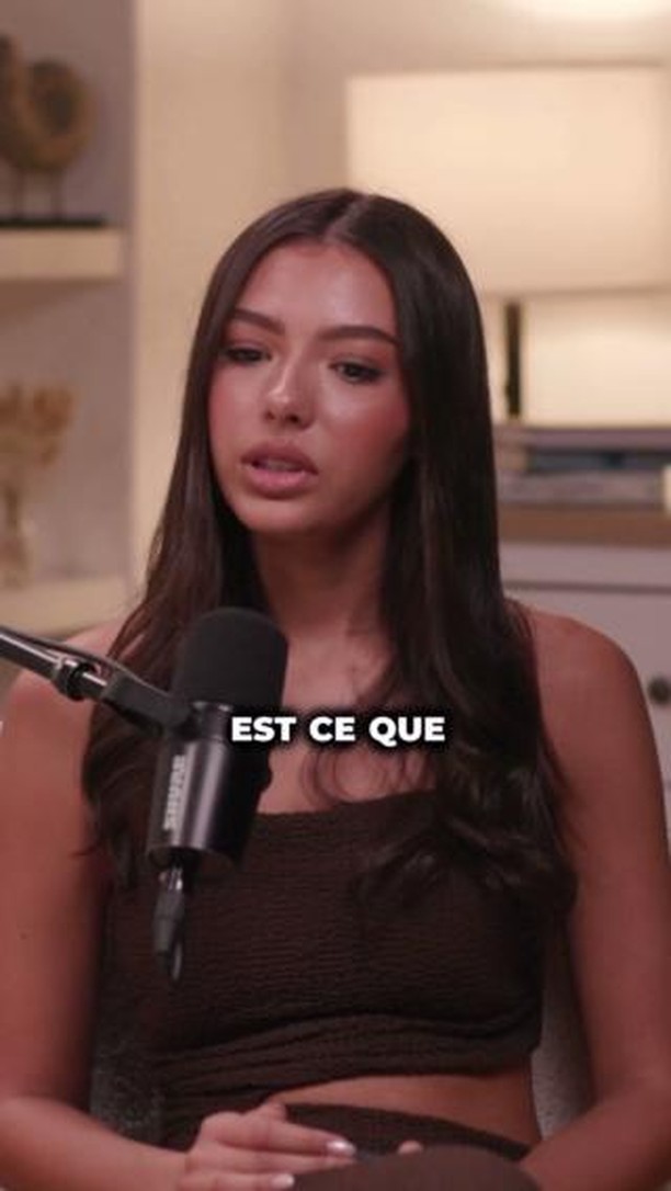 A cover image featuring a woman in a brown top speaking into a black microphone. The overlay text, 'EST CE QUE', is positioned below her face, and she's in a well-lit indoor setting. The layout is simple, focusing on the woman.
