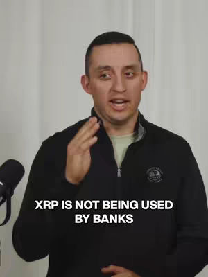 A man with short dark hair and a black jacket is speaking directly at the camera with a serious expression. The background is a white wall. Text overlayed on the image reads, "XRP IS NOT BEING USED BY BANKS."