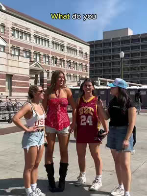 Four young women are standing outside on a sunny day, likely on a college campus. They are posing for the camera against the backdrop of a large brick building. The hook text in yellow, says “What do you”.