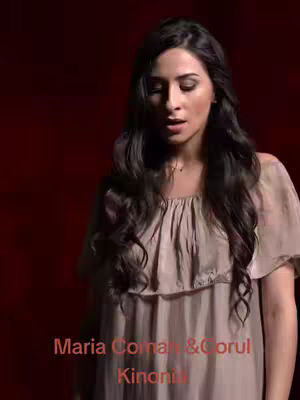 A woman with long dark hair and a light-colored dress sings against a deep red background. Text overlays appear at the bottom, naming the performers.