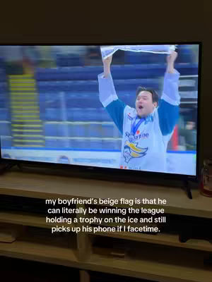 A television screen displays a man holding a trophy with arms raised in celebration. Below the screen, a wooden shelf holds the TV and a small glass jar. The caption on the lower portion of the screen details the characteristics of the person in the image..