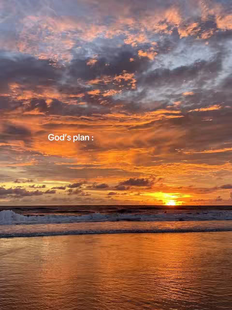 A vibrant sunset over the ocean at the beach. The sky is filled with shades of orange, yellow, and pink, with clouds scattered throughout. The ocean reflects the colors of the sky. The foreground is the sandy beach. There is text that says: God's plan: