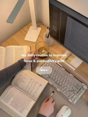The image shows a cozy workspace with a desk, books, a laptop, a cup of coffee, and a mouse. Hands are visible holding a pen and a book. There's a focused atmosphere with a warm color palette.