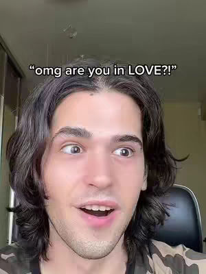 A close-up shot of a young man with long, dark hair looking surprised. Text overlay suggests a question about love. The background is a blurred interior.