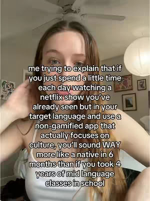 A selfie-style shot featuring a young woman with light skin and long brown hair. She's looking towards the camera. The background includes a room with a ceiling fan, artwork on the wall, and a hanging light. White text is overlaid on the image.