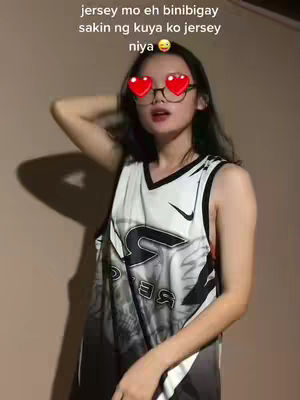 A young woman is posing in a casual indoor setting, wearing a basketball jersey. She is holding up her right arm, with her hand on her head. Her face is framed with heart-shaped glasses, and text appears across the top of the image.