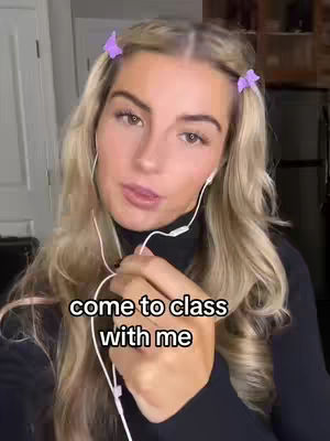 A young woman with long blonde hair, styled in pigtails with purple butterfly clips, looks directly at the camera. She wears a black turtleneck and white earbuds. The image is well-lit, with a soft focus on her face.