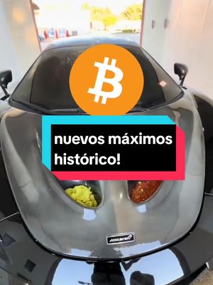 The cover image features a black McLaren sports car, shot from a low angle that emphasizes its sleek design and curves. A superimposed Bitcoin logo, a large orange circle with the Bitcoin symbol in white, floats in the center above the car's hood. Below the Bitcoin symbol, a rectangular text overlay in a teal and red color scheme reads "nuevos máximos histórico!" The background subtly suggests a car wash environment, with reflective surfaces and ambient lighting. The composition is dynamic, using the car's lines and the bold Bitcoin graphic to draw the viewer's eye, and it delivers a sense of opulence, speed, and financial excitement.