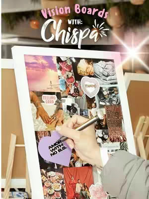 Cover image features a vision board propped on a wooden easel. The vision board is filled with various cutout images and text elements, including pictures of hands, food, and travel destinations. A hand is holding a pen and writing on a purple heart-shaped sticky note. The background includes a blurred arrangement of decorative items and a white wall. The text overlay reads "Vision Boards with: Chispa".