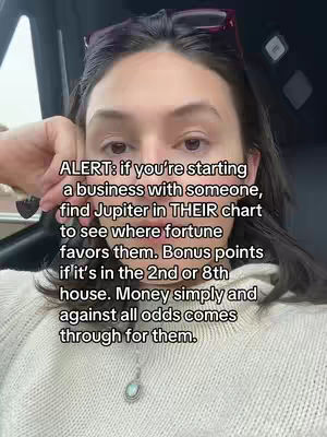 A selfie-style shot featuring a woman with brown hair holding a hand near her face. She has glasses on, pushed up on the top of her head. The background is a car interior. Text overlays the image, offering advice related to business and astrology.