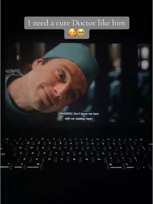 A movie screen displaying a man in a medical cap, with overlaid text and emojis. A laptop keyboard is visible at the bottom of the frame.