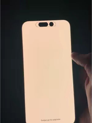 The image shows a close-up of a smartphone screen, presumably an iPhone, turned on against a dark background. The screen emits a soft, warm light that fills the frame. A finger is poised near the edge of the phone, suggesting interaction or a swipe gesture. At the bottom of the screen, the words "Swipe up to upgrade" are faintly visible.