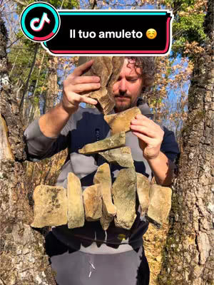 A man is holding pieces of rock in his hands creating a central structure composed of stacked stones against a natural background of trees. The cover image is overlaid with a text box with the text overlay in Italian.