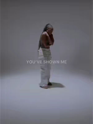 A woman is captured in a medium shot, standing in a softly lit, expansive white space. Her attire consists of a sleeveless top and loose, flowing pants. She’s positioned slightly off-center, with her head inclined and arms crossed in a gesture that conveys introspection. Below her, large white text states 'YOU'VE SHOWN ME'.