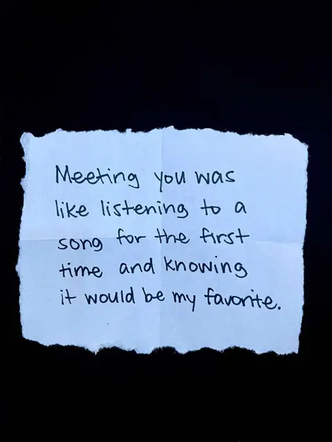 A piece of white paper with uneven edges, seemingly torn from a larger sheet, is centered against a black background. The paper is folded into a rough square with creases. Handwritten in black ink are the words "Meeting you was like listening to a song for the first time and knowing it would be my favorite."