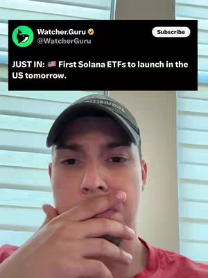 A man in a red shirt and a black cap holds his hand to his mouth while looking at the camera. Behind him is a screenshot of a Twitter post.